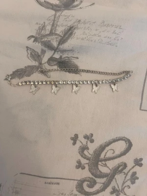 Silverfärgat fot armband  med fjärilar - Snyggt fot armband i silverfärg med gnistrande stenar och små fjärilsberlocker. Kedjan är tunn och justerbar, vilket gör det enkelt att anpassa längden. Perfekt accessoar för dig som gillar detaljer och vill ha något som sticker ut lite extra.