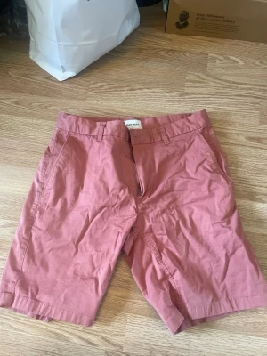 Rosa shorts från EAST WEST - Säljer ett par snygga rosa shorts från EAST WEST. De har klassisk passform med fickor på sidorna och hällor för bälte. Perfekta för varma dagar och enkla att matcha med olika stilar. Orginalpris ca 899