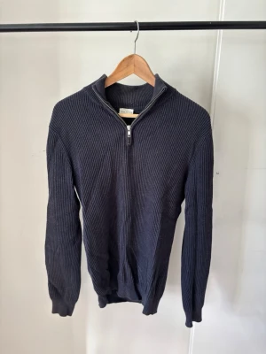 John Henric - Zip tröja  - Mörkblå stickad tröja med ribbad struktur och halv dragkedja framtill. Tröjan har hög krage och långa ärmar, perfekt för lager på lager. Passar till både jeans och chinos för en avslappnad look.