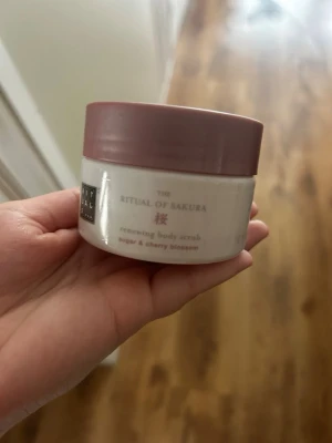 Rituals Sakura body scrub - Säljer en Rituals The Ritual of Sakura renewing body scrub med socker och körsbärsblom. Burken är vit med ett ljusrosa lock och har en rund form. Perfekt för att exfoliera huden och få en fräsch känsla.