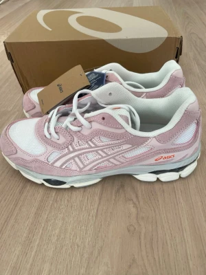 ASICS rosa och vita sneakers - Snygga sneakers från ASICS i en fräsch kombination av ljusrosa och vitt. Skorna har meshpaneler för bra andningsförmåga, detaljer i mocka och syntet samt klassisk ASICS-logga på sidan. Sulan är vit med svarta och grå inslag för en sportig look.