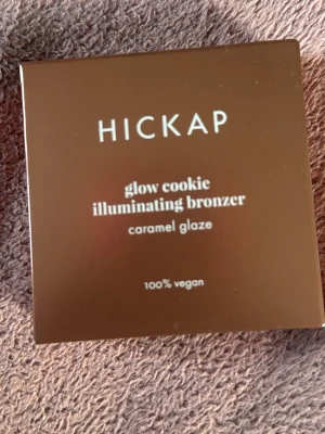 Hickap Glow Cookie Bronzer Caramel Glaze - Glow Cookie Illuminating Bronzer från Hickap i nyansen Caramel Glaze. Kommer i en rund, vit dosa och en brun kartong. Produkten är 100% vegansk och ger en varm, glödande finish till huden. Helt oanvänd säljer den för att den inte passade min hudfärg