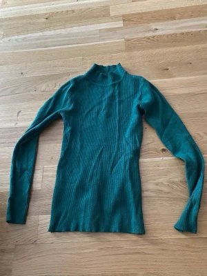 Grön ribbad polotröja från SHEIN - Mörkgrön ribbstickad polotröja från SHEIN i storlek S. Tröjan har lång ärm, figurnära passform och hög krage. Materialet är 50% viskos, 28% polyester och 22% polyamid vilket gör den mjuk och stretchig.