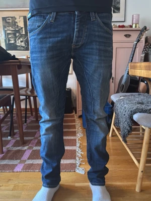 Jack and Jones Slim Glenn  - Säljer ett par blå slim fit jeans med snygga tvättade detaljer och klassiska fem fickor. Jeansen har normal midja och raka ben, samt kontrastsömmar för en cool look. Perfekta för dig som gillar en avslappnad men ändå stilren stil.