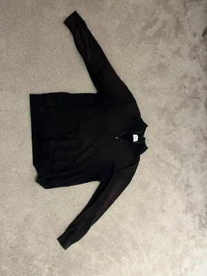 Svart halvzip tröja från Bläck - Stilren svart tröja från Bläck med halvzip och hög krage dock lite solskadad som man ser på bilderna men inget som förstör plagget. Perfekt för lager på lager och enkel att matcha med olika outfits. Tillverkad i mjukt material som känns skönt mot huden. Långärmad modell som passar året runt.