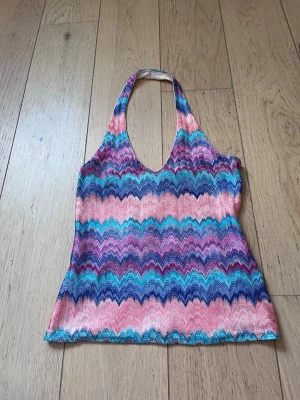 Färgglad mönstrad halterneck topp - Säljer en färgglad halterneck topp från New Look med zigzag-mönster i rosa, blått, turkost och lila. Toppen har en djup v-ringning och är ärmlös, perfekt för sommarens alla tillfällen. Materialet känns mjukt och stretchigt.