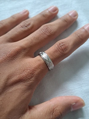 Silverfärgad ring med mönster - Säljer en stilren silverfärgad ring med graverat geometriskt mönster runt om. Ringen har en klassisk, rund form och är tillverkad i metall. Perfekt för dig som gillar enkla men snygga accessoarer.