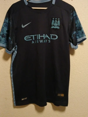 Manchester City Silva matchtröja - Snygg Manchester City matchtröja från Nike med Silva och nummer 21 på ryggen. Tröjan är mörkblå med ljusblå detaljer och mönstrade ärmar. Tillverkad i Dri-FIT material som andas, perfekt för fotboll eller träning. Etihad Airways-logga på bröstet.