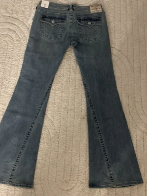 Ljusblå bootcut jeans från true religion - Säljer ett par ljusblå bootcut jeans från Miss Me med klassiska fickor bak och snygga detaljer. Jeansen har en utsvängd passform och är tillverkade i mjuk denim. De är förr stora för mig och kan inte skicka tbx. Köpte för 1299kr säljer för 850kr. Priset kan diskuteras. 