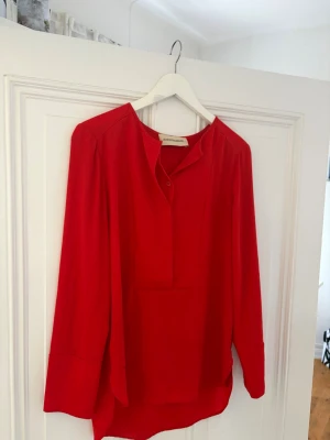 Röd blus från By Malene Birger - Snygg röd blus från By Malene Birger med avslappnad passform och rundad halsringning. Blusen har knäppning framtill och långa ärmar. Tillverkad i ett mjukt, lätt tyg som ger ett elegant fall.
