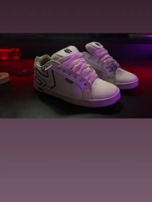 Vita Etnies sneakers med svart detalj - Säljer ett par klassiska vita Etnies sneakers med svart logga och detaljer på sidan. Skorna har lågt skaft, tjock vit sula och vita skosnören. Perfekta för dig som gillar skate-stil och vill ha något stilrent men ändå street.