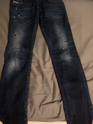 Äkta mörkblåa diesel jeans. Pris kan sänkas - Säljer ett par mörkblå jeans med slitningar och hål på båda benen. Jeansen har klassisk femficksmodell, raka ben och kontrastsömmar. Perfekta för en avslappnad och trendig look. Materialet är denim i bomull.