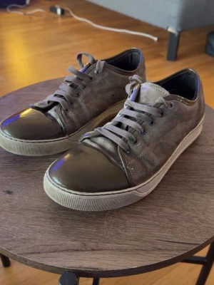 Lanvin skor - Snygga grå sneakers med ovandel i mocka och tåparti i glansigt lackmaterial. Skorna har matchande grå skosnören och vit sula. Perfekta för dig som gillar en stilren men ändå unik look.