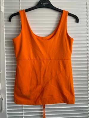 Orange sportlinne från SATS Sports - Snyggt orange sportlinne från SATS Sports med breda axelband och rundad halsringning. Tillverkat i ett stretchigt funktionsmaterial som passar perfekt till träning. Tryck med logga och texten 'Keep Moving' nertill. Perfekt för gymmet eller löprundan.