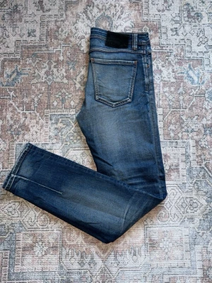 Mörkblå slim fit jeans - Snygga mörkblå slim fit jeans med klassisk femficksdesign och diskreta slitningar. Jeansen har en rak passform och kontrastsömmar som ger en stilren look. Perfekta för dig som gillar en enkel men trendig stil.