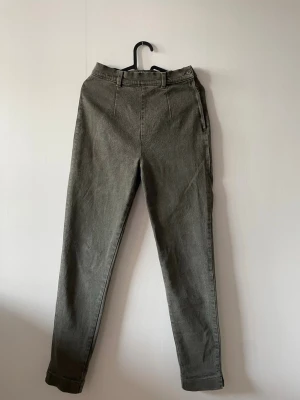 Gröna raka jeans med hög midja - Snygga gröna jeans med hög midja och raka ben. Jeansen har bälteshällor, knappstängning och diskreta sömdetaljer framtill med knäppning i sidan. 