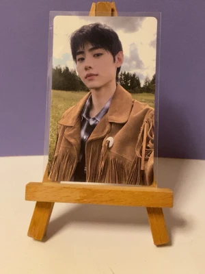 ENHYPEN Border: Day One photocard Sunghoon  - Exklusiv photocard från ENHYPENs album Border: Day One. Kortet har en bild på en medlem i brun mockajacka med fransar och blå skjorta, och levereras i plastficka. Perfekt för samlare av K-pop merch.