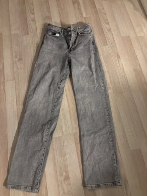 Grå raka jeans från Woodbird - Säljer ett par grå jeans från Wood Wood i rak modell. Jeansen har klassisk femficksdesign, knappgylf och är tillverkade i ett slitstarkt denimtyg. Perfekta för dig som gillar en clean och enkel stil.