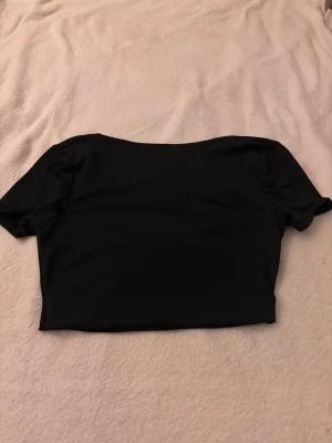 Svart topp - Snygg svart croppad topp med omlottdetalj bak och korta ärmar. Perfekt för att styla med höga jeans eller kjol. Enkel och stilren design som passar till många olika looks.