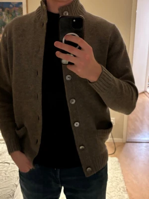 Alan paine cardigan - Säljer en brun kofta med hög krage och stora knappar framtill. Koftan har ribbade muddar vid ärmslut och nederkant samt två fickor fram. Perfekt för lager på lager och enkel att matcha med olika outfits. Nypris 2500kr