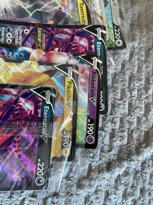 Pokémon V-kort samling - Samling med flera Pokémon V-kort, bland annat Pikachu V, Eternatus V, Alakazam V och Toxtricity V. Korten har färgstarka motiv och holografisk yta. Perfekt för dig som gillar att samla eller spela Pokémonkort.