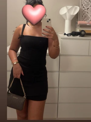 Svart kort klänning - Kort svart klänning med rosettdetaljer och dragkedja från Pull & Bear i storlek S. Använd en gång