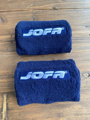 Marinblå handleds skydd  från Jofa - Ett par marinblå handleds skydd från Jofa i mjukt och stretchigt frottématerial. Perfekta för träning eller sport, med broderad logga i vitt framtill. Sitter skönt runt handleden och absorberar svett effektivt.