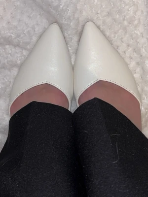 Vita spetsiga ballerinaskor - Säljer ett par vita klackskor med spetsig tå och tunna remmar som korsas över foten. Skorna är helt oanvända att och passar mycket bra på fest, student eller bal.