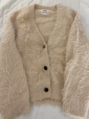Beige/ljusrosa fluffig kofta från Monki - Säljer en supermjuk och fluffig beige kofta från Monki. Koftan har v-ringning och stora svarta knappar. Storlek XXS men skulle säga att den passar mer XS/S. Helt ny, nästan aldrig använd. 