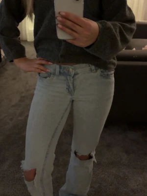 Ljusblå lågmidjade bootcut jeans från Nelly - Säljer ett par ljusblå lågmidjade bootcut jeans och slitningar vid knäna. Jeansen har cool broderad detalj i rosa på bakfickorna och klassisk femficksmodell. 