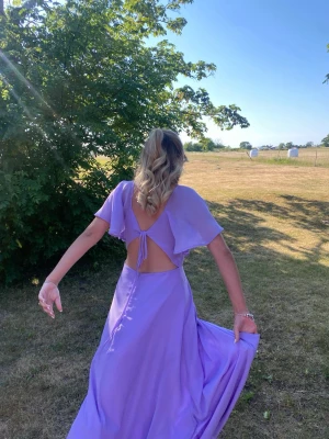 Ljuslila långklänning med öppen rygg - Säljer min ljuslila långklänning med korta ärmar och öppen rygg med knyt. Jag har använt den en gång💕