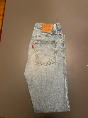 Levi's 501 ljusblåa jeans  - Klassiska ljusblå Levi's jeans med rak passform och hög midja. Jeansen har en bakficka med den ikoniska röda Levi's-lappen och är gjorda i slitstark denim. Perfekta för en avslappnad och tidlös stil.