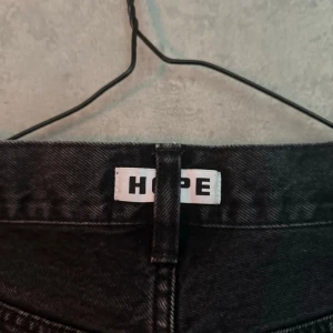 Hope Wide Jeans - Säljer ett par HOPE jeans i svart tvätt. Klassisk 5-pocket-modell med clean uttryck och den där typiska HOPE-balansen mellan minimalistiskt och edgy. Funkar lika bra uppklätt med boots som mer avslappnat med sneakers. 🔹 Märke: HOPE 🔹 Färg: Svart / urtvättad svart 🔹 Modell: Rak / lätt avslappnad passform 🔹 Detaljer: Knapp med HOPE-branding, klassisk 5-pocket, patch bak 🔹 Tillverkning: Made in Portugal 🔹 Skick: Bra