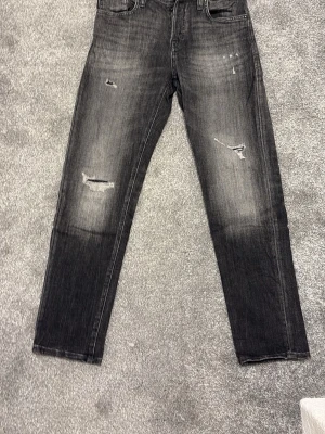 Svarta slitna jeans - Säljer ett par svarta jeans med slitningar och tvättad look. Jeansen har raka ben och klassisk femficks design. Storlek 29/30.