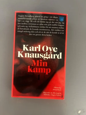 Min kamp 1 av Karl Ove Knausgård - Romanen 'Min kamp 1' av Karl Ove Knausgård har ett omslag i svart och rött med tydlig vit och röd text. Boken är tryckt i pocketformat och utgiven av Norstedts. Omslaget har citat och recensioner tryckta på framsidan.