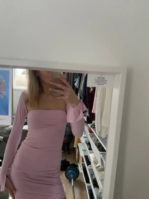 Ljusrosa offshoulder kort klänning - Trendig ljusrosa kort klänning med offshoulder-design och långa ärmar. Klänningen har en tight passform och är tillverkad i ett mjukt stretchigt material som framhäver figuren. Perfekt för dig som vill ha en stilren och modern look.