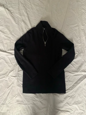 Svart stickad tröja med halvzip - Säljer en svart stickad tröja från Only & Sons med halvzip och hög krage. Tröjan har lång ärm och är ribbstickad vilket ger en snygg struktur. Perfekt för lager på lager och enkel att matcha med olika outfits.