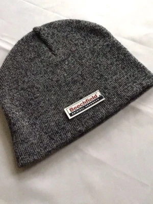 Mörkgrå mössa från Beechfield - Snygg mörkgrå melerad mössa från Beechfield med en patch framtill där märket står. Klassisk och enkel design i mjukt stickat material som passar perfekt till kalla dagar.