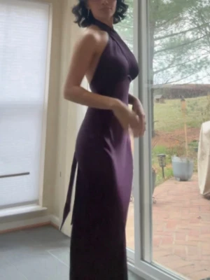 Lång lila satinklänning med öppen rygg - Säljer en elegant långklänning i glansigt lila satin med halterneck och snygg omlott-detalj framtill. Klänningen har öppen rygg med knytband och figurnära passform som ger en lyxig känsla. Köpt från princesspolly och i perfect skick!