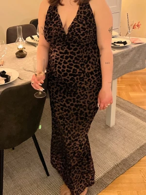 Leopardmönstrad långklänning - Snygg långklänning med leopardmönster och djup v-ringning. Klänningen har ärmlös design och figurnära passform som framhäver siluetten. 