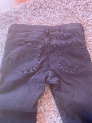 Svarta bootcut jeans med låg midja - Säljer ett par svarta bootcut jeans med låg midja och klassiska bakfickor. Jeansen har bälteshällor och är tillverkade i stretchigt denimtyg för en bekväm passform. Perfekta till en avslappnad eller trendig look.