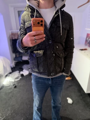 Svart dunjacka från Moncler - Nu har du chansen att förvärva denna perfekta kombinationen av stil och funktionalitet med denna svarta fieldjackan. Denna jacka är designad för den moderna mannen som inte vill kompromissa med varken utseende eller praktiska behov. Med sex rymliga fickor är denna jacka perfekt för att förvara alla nödvändigheter, inklusive kondomer, så att du alltid är redo för en romantisk kväll.den sitter som bäst på dig som är runt 180 cm hög Jackan har infällbara luva i kragen. Hör av dig vid minsta fråga 🔥