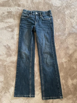 Blå jeans från Kapphal i barnstorlek - Ett par klassiska blå jeans från Kappahl i rak modell. Jeansen har fem fickor, normal midja och snygga kontrastsömmar. Tillverkade i slitstarkt denimtyg som passar perfekt till vardagslooken.