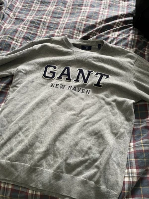 Grå college-tröja från GANT - Snygg grå college-tröja från GANT med broderad text 'GANT NEW HAVEN' i marinblått och vitt på bröstet. Sitter mer som en L på mig som är 180 80kg. Liten i storleken alltså 