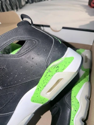 Svarta och limegröna Air Jordan sneakers - Säljer ett par snygga Air Jordan sneakers i svart läder med limegröna detaljer och vit sula. Skorna har den klassiska Jumpman-loggan bak och coola gröna inslag med stänkdesign på sulan. Insidan är fodrad i limegrönt tyg för extra kontrast.