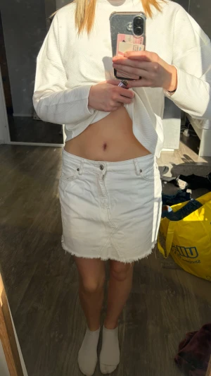 Vit jeanskjol med rå kant - Säljer en vit kort jeanskjol med rå, fransig kant nertill och klassiska fickor både fram och bak. Kjolen har knapp- och dragkedjestängning framtill och är i en enkel, stilren design som passar till det mesta.