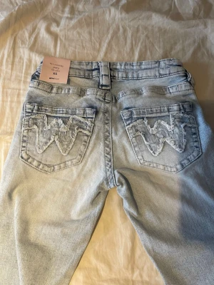 Ginatricot ljusblå bootcut jeans XS, 14+ - Ljusblå bootcut jeans från Ginatricot med broderade bakfickor och låg midja. Jeansen har utsvängda ben. Säljer då jag inte hann returnera i tid, så de är helt oanvända💗Storlek xs 14+ Midjemått tvärsöver: ca 31cm. Pris kan diskuteras!