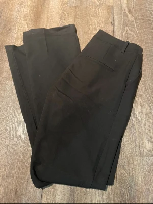 Svarta kostymbyxor från Bik Bok - Snygga svarta kostymbyxor från Bik Bok i klassisk rak modell. Byxorna har diskreta fickor och bälteshällor i midjan. Perfekta för en stilren och clean look. Materialet känns mjukt och följsamt, vilket gör dem bekväma att bära hela dagen.