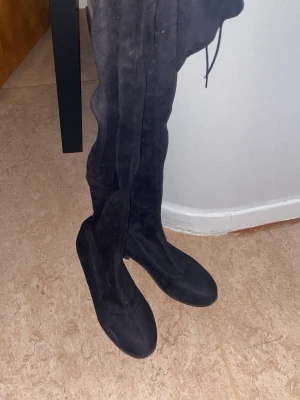 Svarta overknee stövlar i mocka - Säljer ett par svarta overknee stövlar i mjuk mocka med snörning upptill. Stövlarna har en smal passform och rund tå.