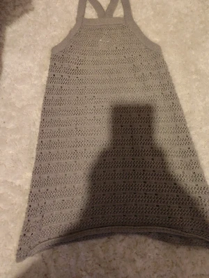 Beige stickad kortklänning - Säljer en grå stickad klänning med hålmönster och breda axelband. Klänningen har en rak passform och är perfekt för varma dagar att ha över badkläder. Materialet är mjukt och luftigt stickat, vilket ger en avslappnad och trendig look.